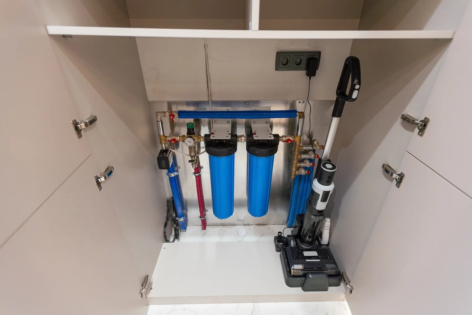 Whole-home water filtration system with twin cartridge housings mounted inside a utility cabinet