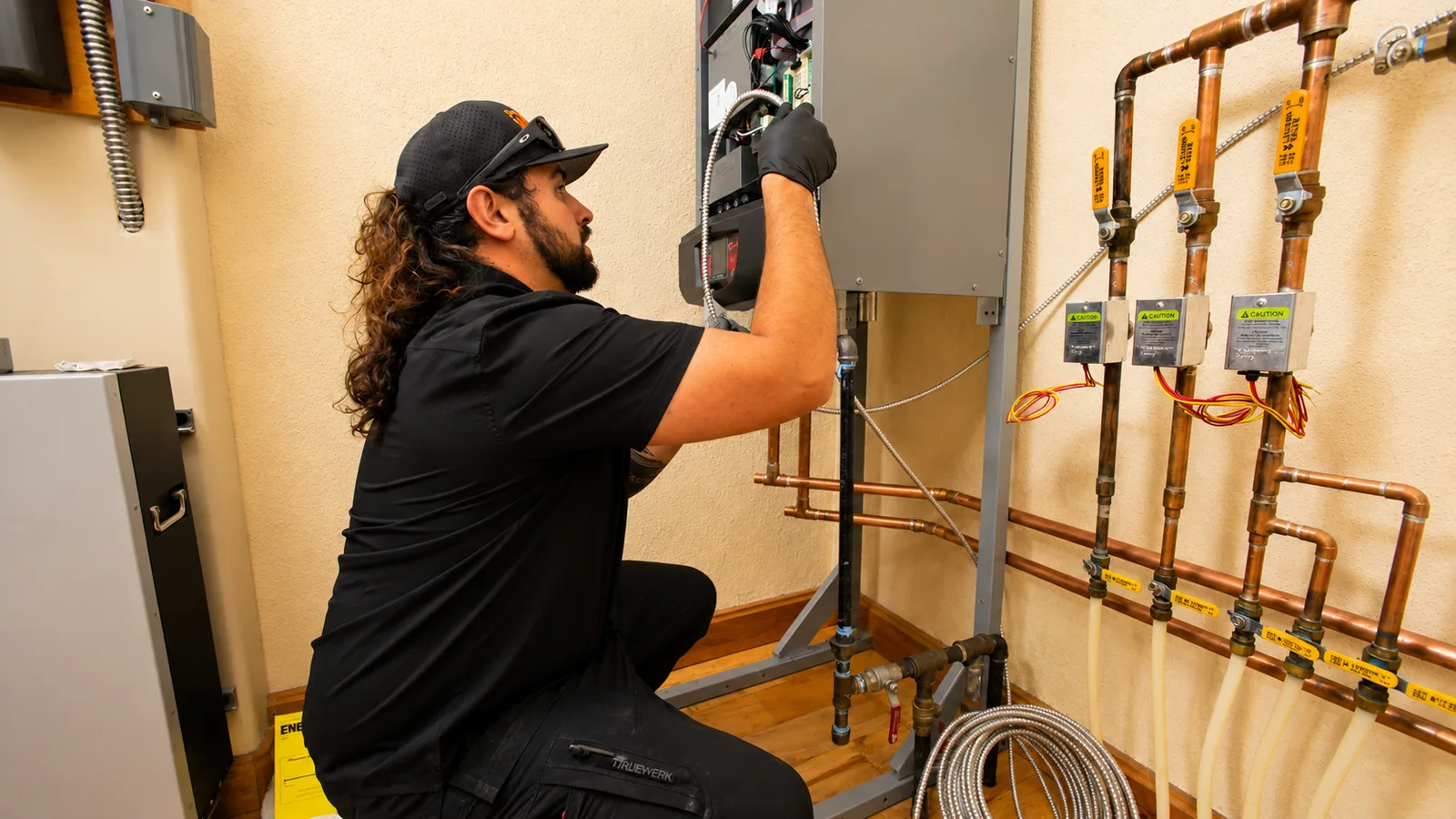 EP Plumbing, Heating & Air technician servicing a boiler control panel beside a copper gas manifold